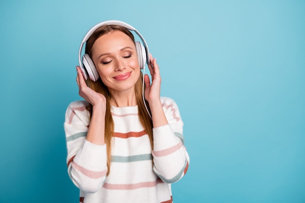 Photo of cheerful woman with eyes closed charming pretty sweet in headphones listen to music near empty space isolated pastel color wall