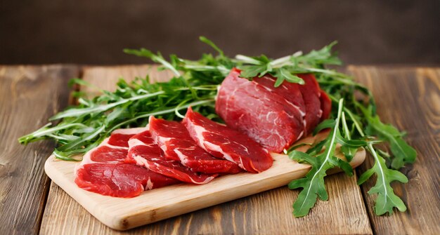 photo chef knife next to big chunks of red meat and green vegetables on wooden table