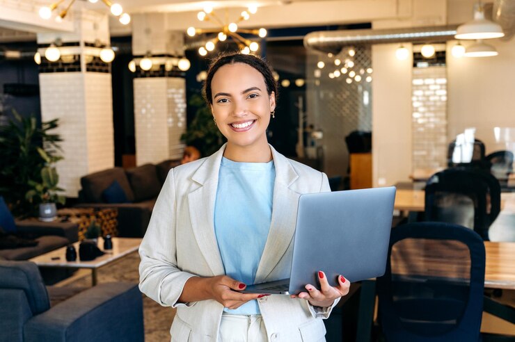 Photo photo of a confident beautiful elegant young mixed race woman successful company worker seo programmer standing in her office holds an open laptop looking at the camera smiling friendly