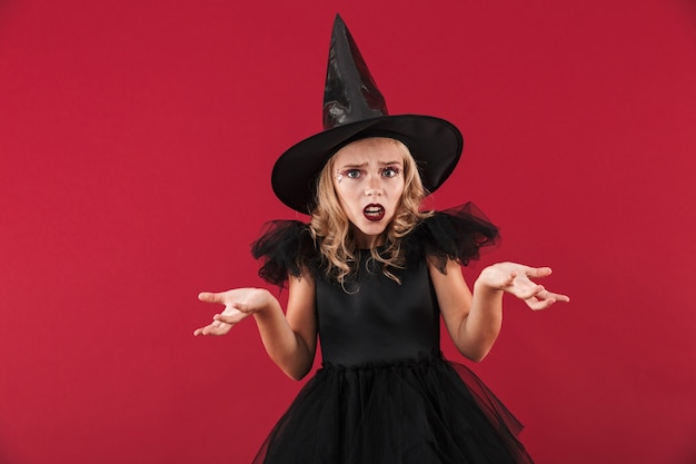Фото сбитой с толку маленькой девочки-ведьмы в карнавальном костюме на хэллоуин