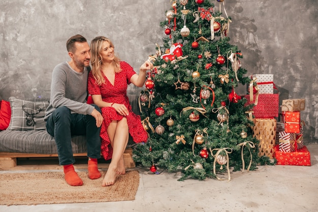 Photo of Cozy Happy Evening Young Couple at Home, Christmas Decor, Red Green Shades, Woman and man with gift box.