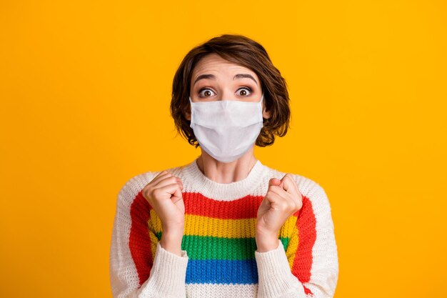 Photo of crazy excited girl hold fists astonished wear facial mask striped pullover isolated yellow color background