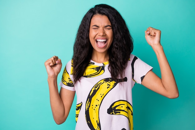 Photo of crazy young black girl raise hands open mouth eyes closed wear banana print t-shirt isolated turquoise color background