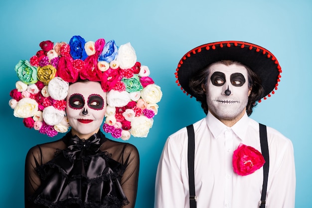 Photo of creepy monster couple man lady playful look zombie first meet after resurrection wear black dress death costume roses headband suspenders sombrero isolated blue color background