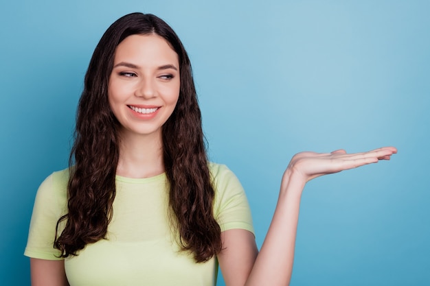 Photo of curious promoter girl palm hold blank space look side think on blue background