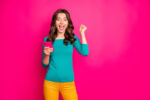 Photo photo of curly cheerful positive nice charming excited girl ecstatic about feednews she read wearing yellow pants trousers green shirt expressing amazement on face isolated vivid pink color background