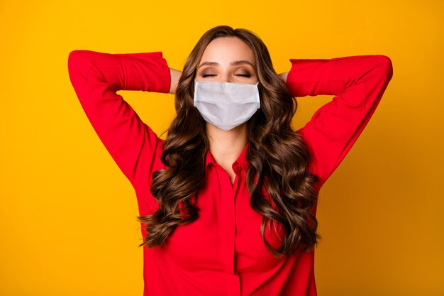 Photo of curly lady hold hands behind head eyes closed break relax meditate enjoy covid quarantine formalwear red office shirt medical mask isolated bright yellow color background