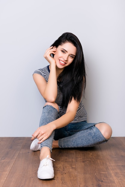 Photo of cute attractive young smiling woman with long hair and striped shirt sittind on the floor