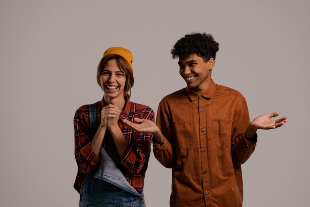 Photo of cute couple farmers laugh and look happy together . White woman wears denim overall, black man shirt isolated grey color background.