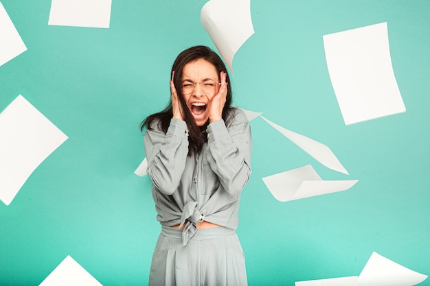 Photo photo of cute female in glasses is screaming, paper is flying around her