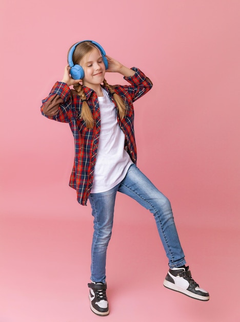 Photo of a cute funny young teenage girl in a pink jumper headphones dancing enjoying music on a background