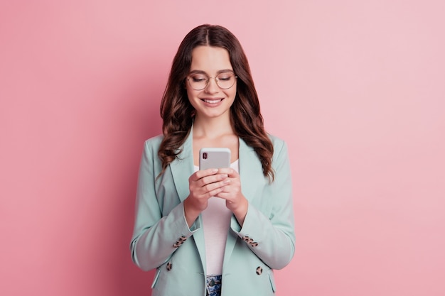 Foto di una signora carina che tiene il telefono in chat mentre scrive messaggi in posa su sfondo rosa