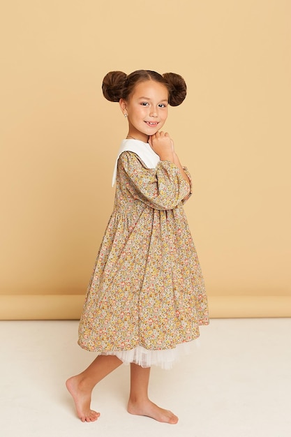 Photo of a cute little beautiful girl in the studio on a brown background. The girl is dressed in a lush yellow dress, looks at the camera and smiles. Art photography. Autumn photo shoot..