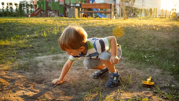 公園に座って砂を掘るかわいい幼児の男の子の写真