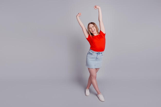 Photo of cute pretty cheerful lady enjoy stretching wear red tshirt jeans mini skirt isolated on grey background