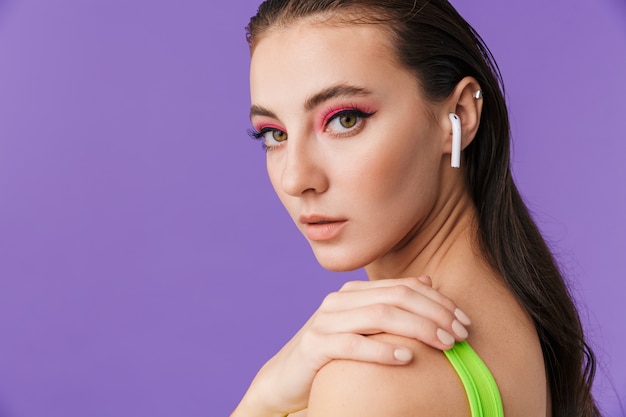 Photo of cute young woman with bright makeup using earpods