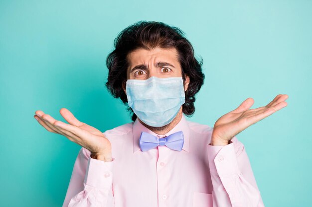 Photo of disappointed guy unsure covid quarantine wear medical mask isolated cyan colored background