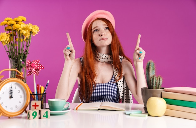 Photo of displeased student girl pointing fingers upward at copyspace while doing homework isolated over purple wall