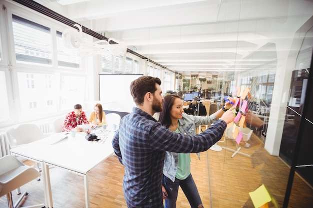 Photo editors looking at sticky notes on glass in meeting room