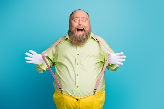 Photo of excited fat man pulling suspenders on blue background