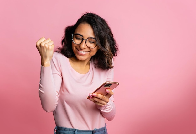 photo excited girl shows mobile phone screen and scream with pink background