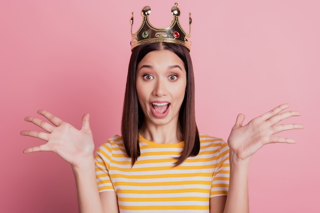 興奮した女の子らしいかわいい女性の王室の反応の写真口を開けて手のひらを上げるピンクの背景に王冠を着用