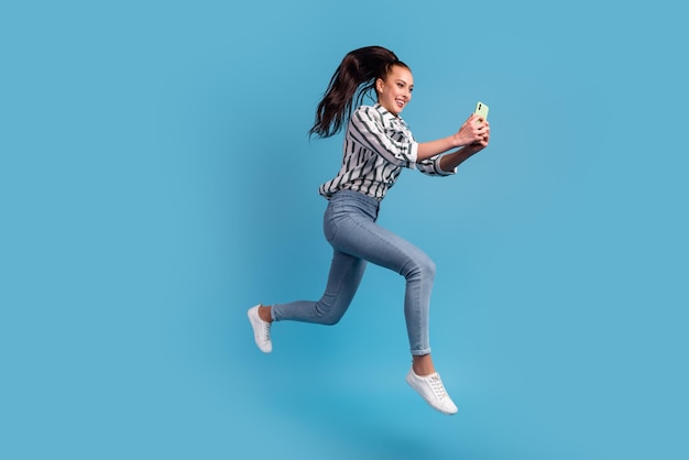 Photo of excited lady dressed shirt using 5g modern device jumping high smiling isolated blue color background