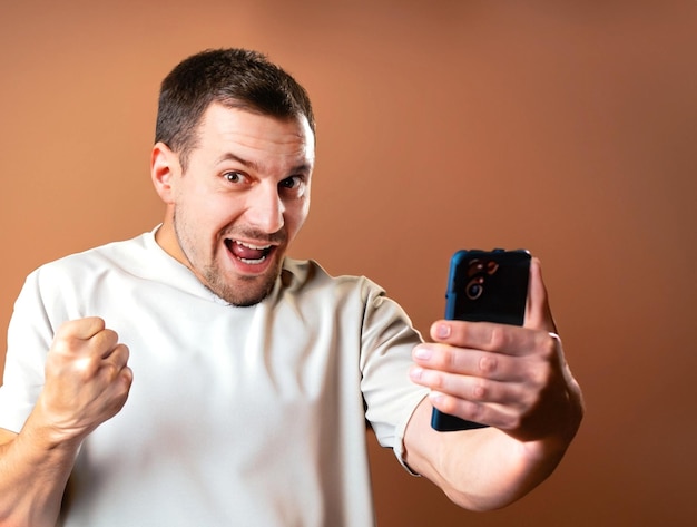 photo excited man shows mobile phone screen and scream with brown background