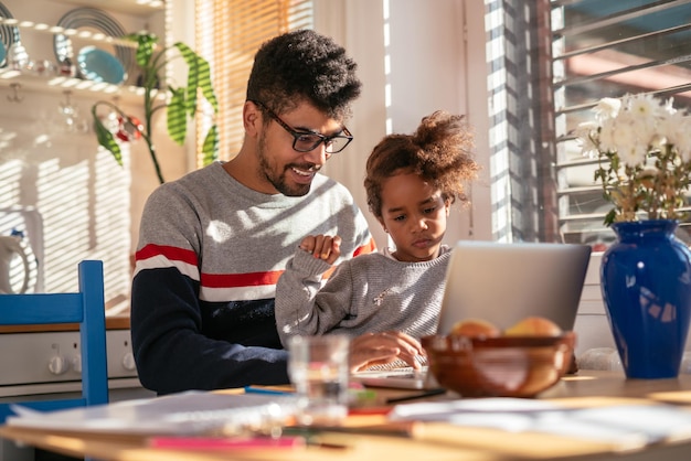 Photo of father and daughter playing on a computer at home She is sitting in his lap