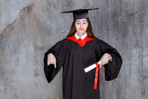 Photo of female student wearing gown pointing at somewhere. High quality photo