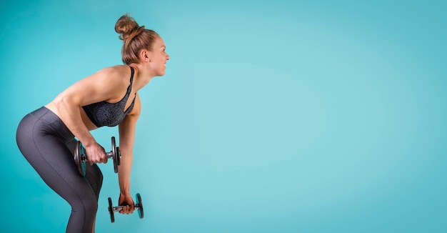 Photo of fitness girl working out with dumbbells on blue background Free space copy space