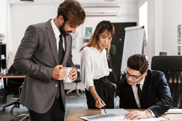 Photo of focused colleagues discussing project and drinking coffee while working in open-plan office