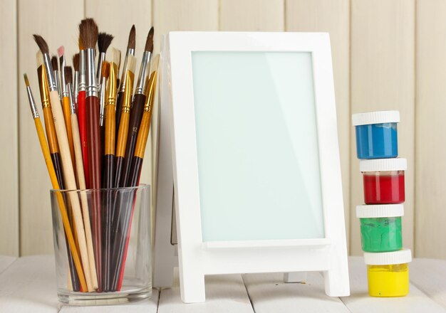 Photo frame as easel with artist's tools on wooden background