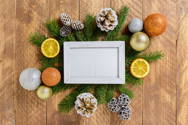 Photo frame between Christmas decoration, with color balls and pine cones on a brown wooden table. Top view, frame to copy space