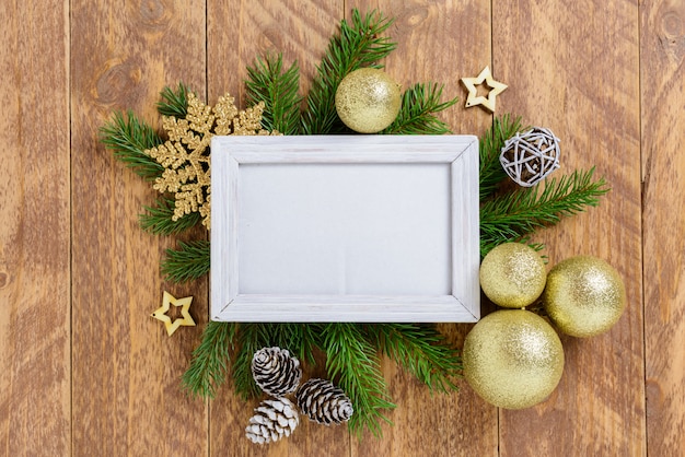 Рамка для фотографий между рождественским украшением, с золотыми цветными шарами и снежинками на коричневом деревянном столе. Вид сверху, рамка для копирования пространства