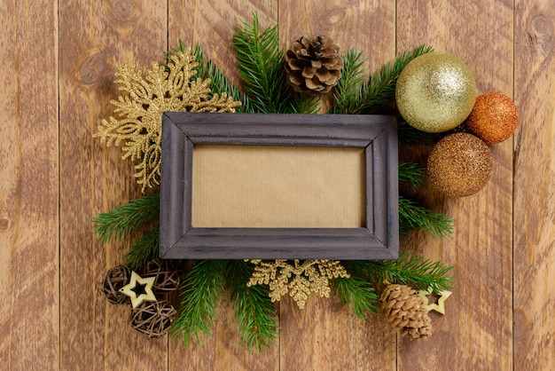 Photo frame between Christmas decoration, with golden color balls and snowflakes on a brown wooden table. Top view, frame to copy space