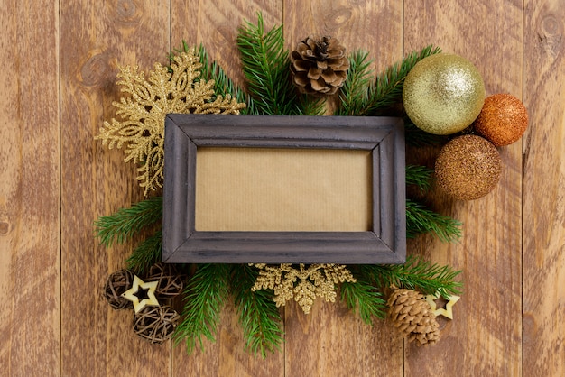 Photo frame between christmas decoration, with golden color balls and snowflakes on a brown wooden table. top view, frame to copy space