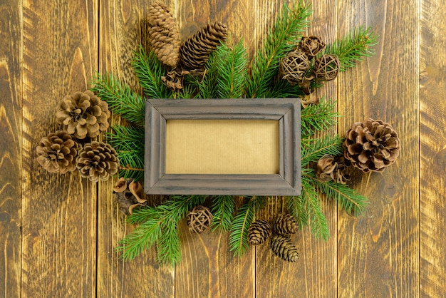 Photo frame between Christmas decoration, with pine cones on a brown wooden table. Top view, frame to copy space.