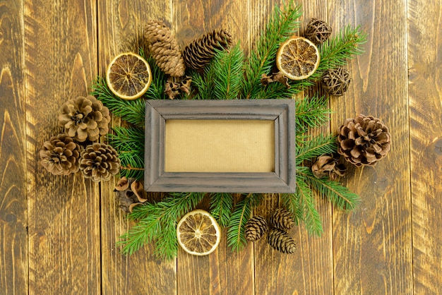 Photo frame between Christmas decoration, with pine cones on a brown wooden table. Top view, frame to copy space.