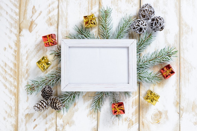 Photo frame between Christmas decoration, with pine cones and gift boxs on a white wooden table. Top view, frame to copy space