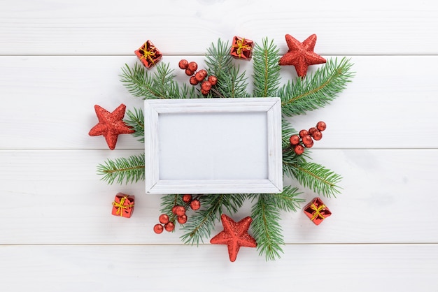 Photo frame between Christmas decoration, with red stars and gift box on a white wooden table. Top view, frame to copy space