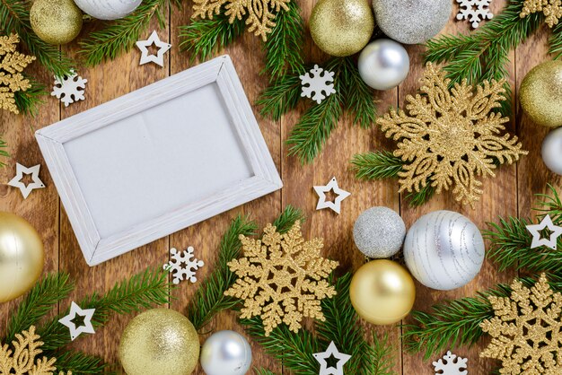 Photo frame between Christmas decoration, with snowflakes and balls on a brown wooden table. Top view, frame to copy space