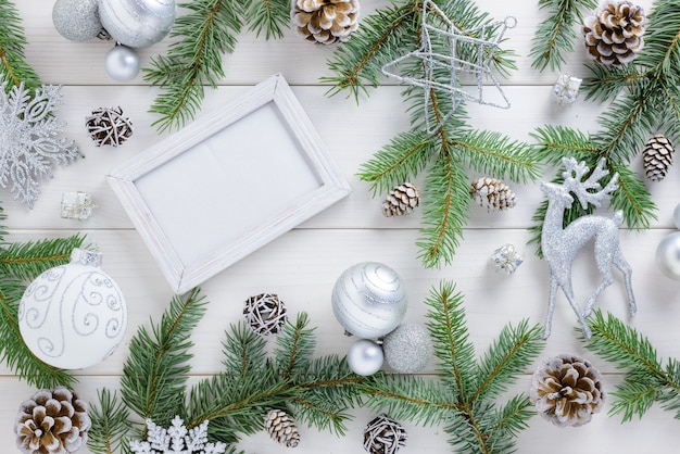 Photo frame between Christmas decoration, with white balls and stars on a white wooden table. Top view, frame to copy space.