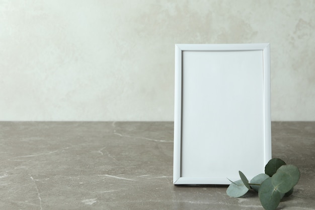 Photo frame and eucalyptus twig on gray textured table against white textured background