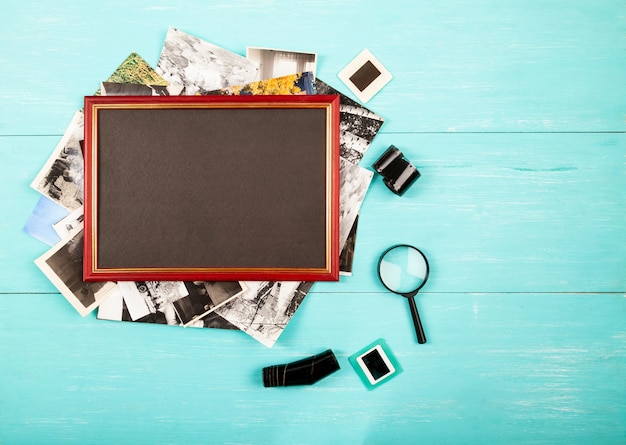 Photo frame and old photos in a stack on blue table, flat lay