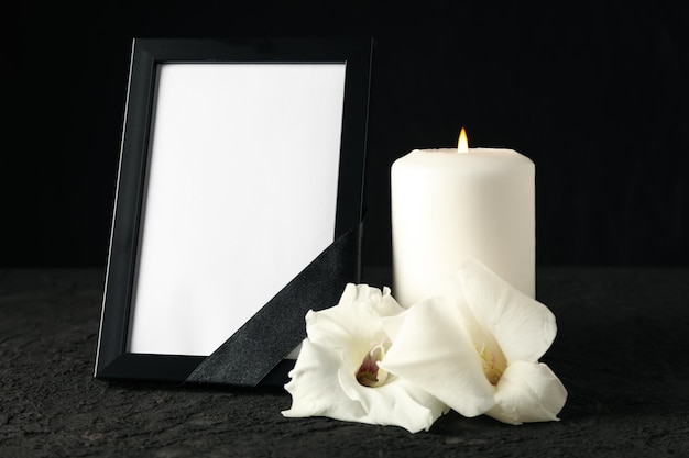 photo frame with black ribbon candle and flowers on black background