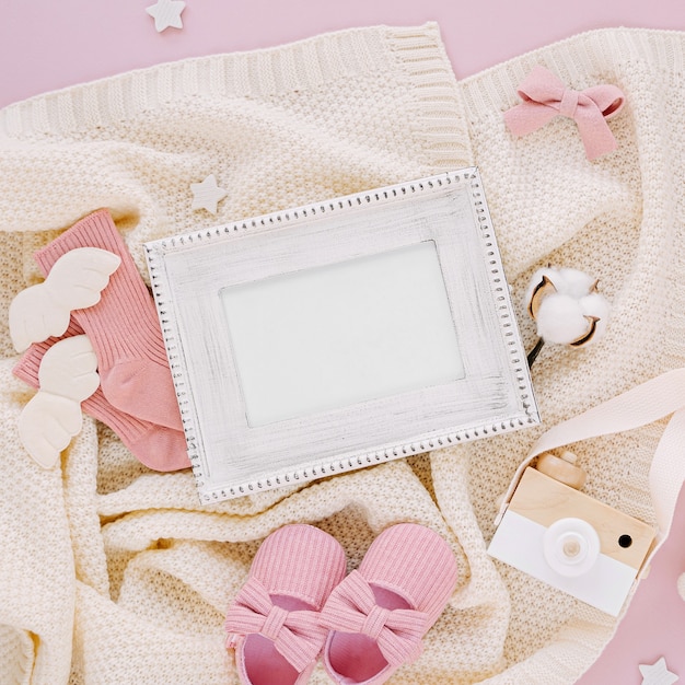 Photo frame with set of clothes and accessories fot newborn. Toys, socks and baby slippers with knitted blanket on pink background. Baby shower concept. Mock up tor text.  Flat lay, top view