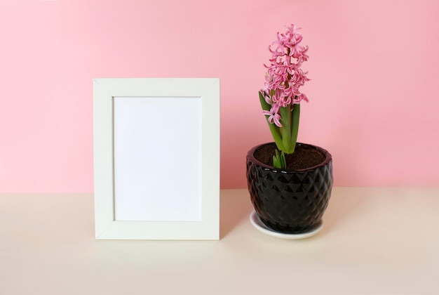 Photo frame with white blank card and flowers on pastel pink background Mock up poster frame Stylish template