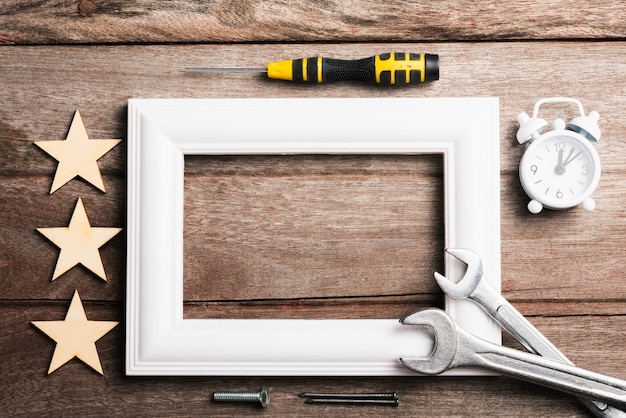 Photo frame with wrenches, stars and alarm clock on wood table, flat lay