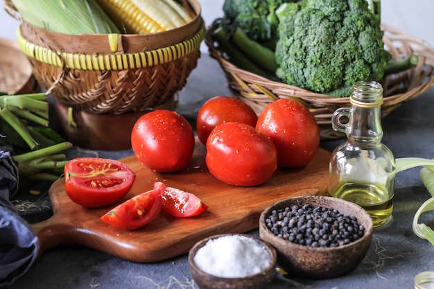 Photo of fresh tomatoes in cutting board, around vegetables, carrot, salt, black pepper, corn, broccoli. Slice tomatoes. Harvesting tomatoes. Wooden table.